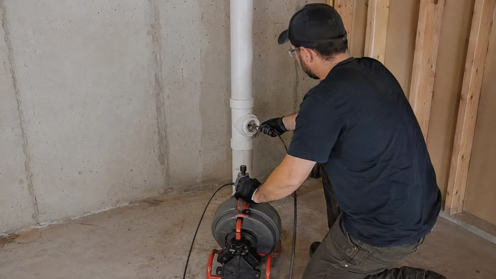 Technician clearing a residential PVC drain cleanout in an unfinished basement